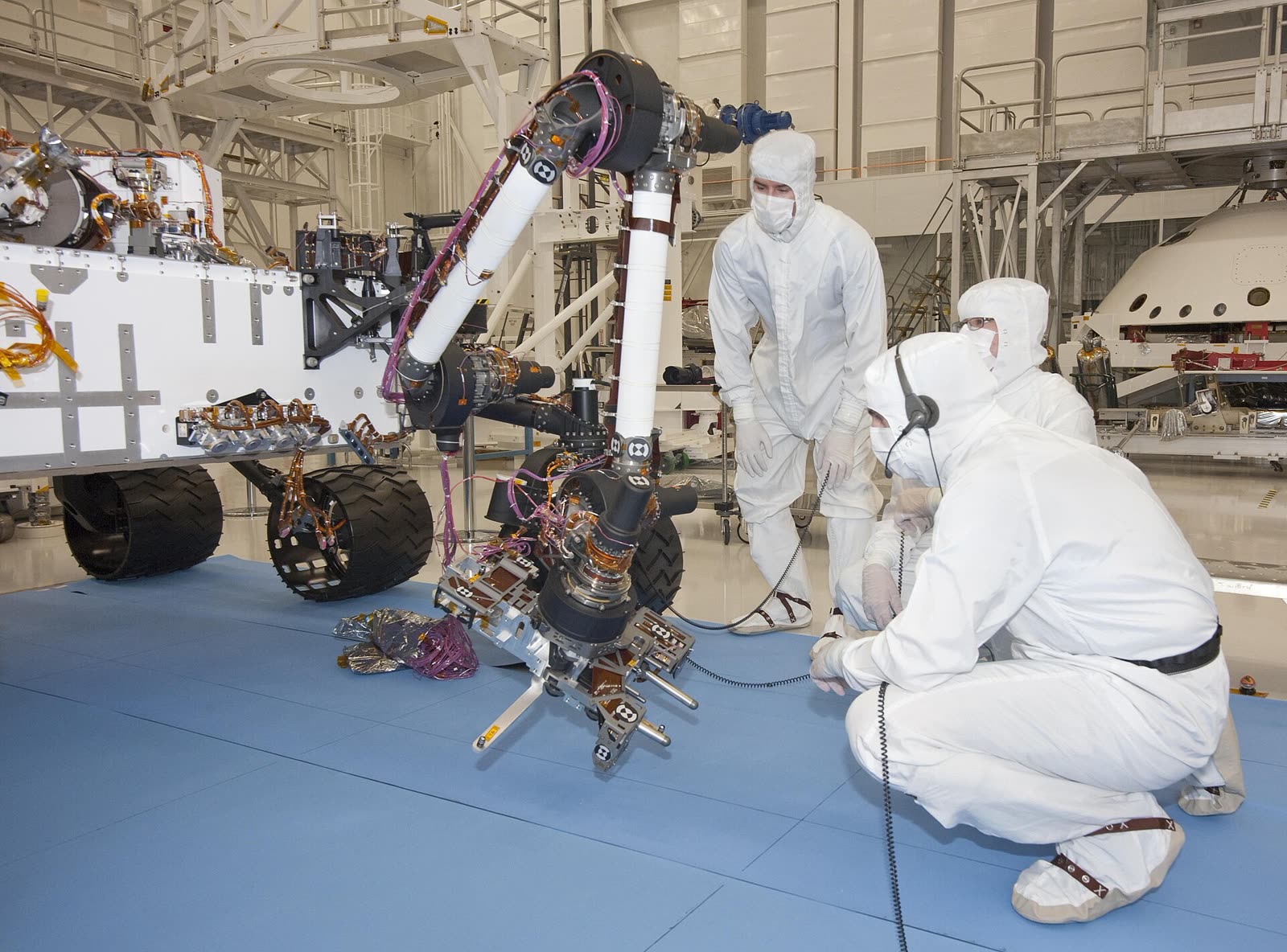 Engineers in clean-room suits testing a planetary rover's robotic arm